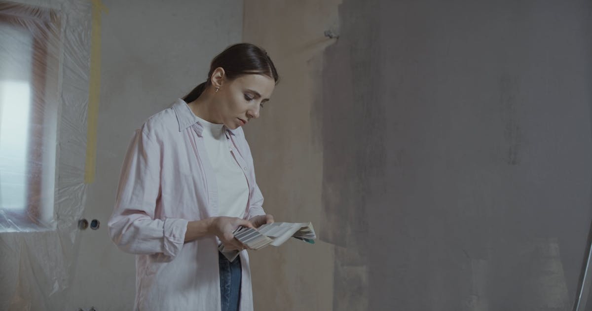 Homeowner checking a sample card against a freshly skimmed wall during a renovation