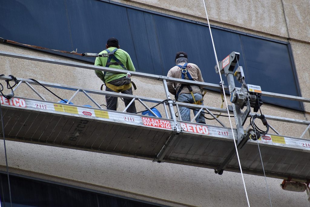 Two workers on a suspended platform along a building facade